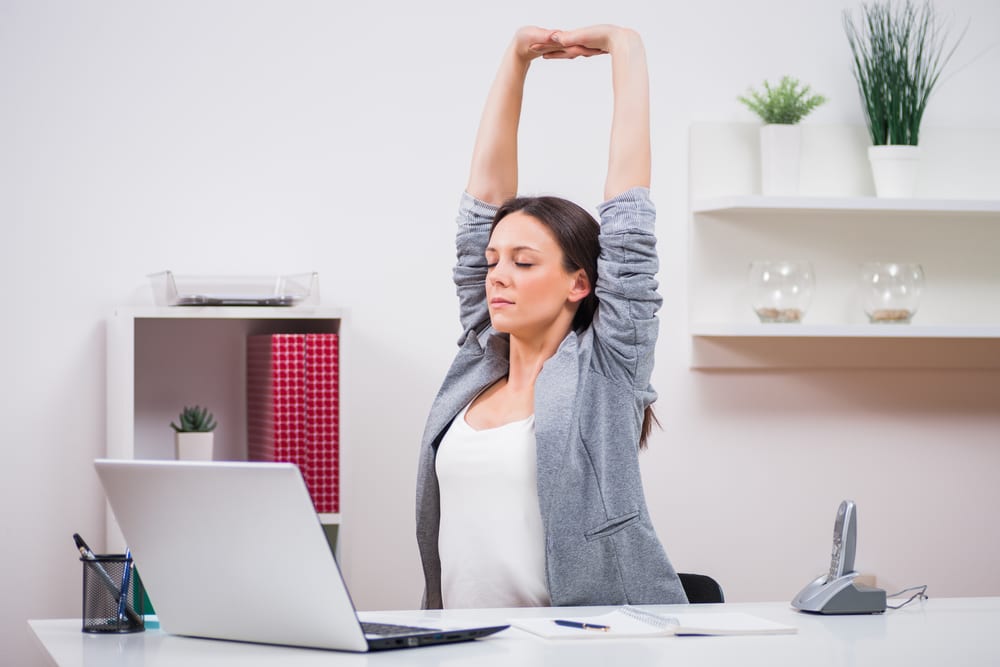 Person practicing gentle stretching exercises at their desk workspace